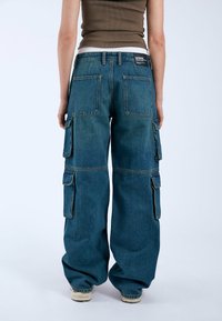 Jeans cargo en denim de azul medio, de corte holgado, con dos bolsillos traseros y dos bolsillos laterales de cargo. Acabados con detalles de costura visibles.