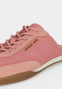 Gros plan d'une basket Michael Kors rose avec des panneaux en daim et en tissu, des lacets roses, des coutures blanches et une semelle marron.