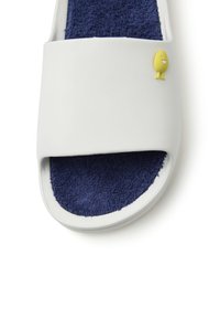 Sandalia deslizante blanca con una plantilla de toalla de rizo en color marino. Presenta un empeine liso y un pequeño acento de personaje amarillo en la correa.