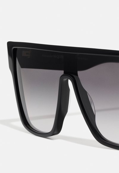 Ochelari de soare negri, de dimensiuni mari, cu ramă pătrată, lentile cu gradient, brațe groase și accente delicate tăiate, fabricate din material plastic durabil.