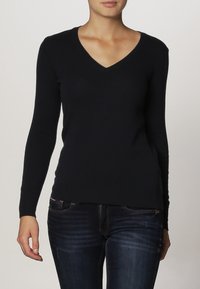 Black v-neck sweater in a soft, stretchy fabric with long sleeves. Features a fitted design and ribbed texture at the hem. Worn with jeans.