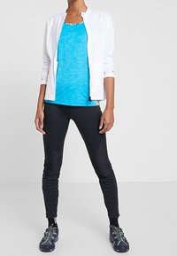 Bílá bunda na zip, světle modrý tílko, černé legíny, tmavé boty s vzorovanými akcenty. Hladké textury a sportovní střih.