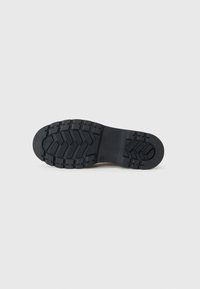Suela de zapato de goma negra con un patrón de relieve profundo, con bordes redondeados y un tacón plano para mejorar el agarre y la durabilidad.