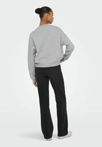 Sudadera gris con cuello redondo, corte relajado y puños acanalados, combinada con jeans negros de campana y zapatillas blancas. Vista trasera del conjunto.