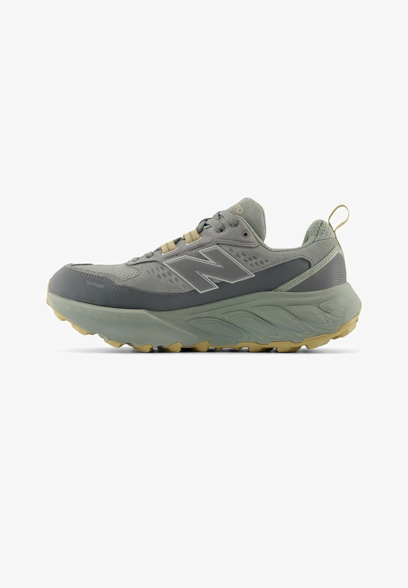 Grauer und beiger New Balance Sportschuh mit dicker Sohle, Schnürung vorne, Lasche an der Ferse und Logo an der Seite.