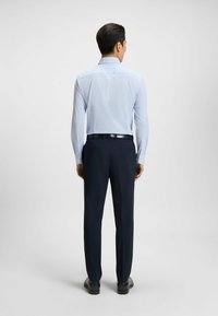 Ljusblå långärmad skjorta med vertikala ränder, matchad med mörkblå byxor. Skjortan har en klassisk krage och knappmuddar.