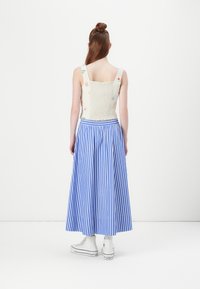 Top scurt brodat cu flori, cu smocking, asortat cu o fustă lungă din rayonne albastră și albă. Modelul poartă teneși albi cu glezna.