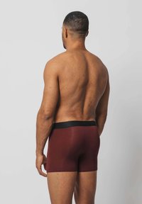 Burgunderfarbene Herren-Boxershorts mit schwarzem elastischem Bund, glatter Textur und enganliegendem Design, von hinten betrachtet.