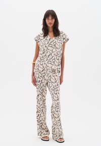 Lichtgewicht stoffen set met een v-hals top en uitlopende broek in crème, met een zwart abstract loof patroon en een losse pasvorm. Gecombineerd met sandalen.