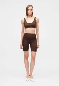 Barna sportos szett, mely illeszkedő crop topból és magas derekú rövidnadrágból áll, rugalmas anyagból, sima textúrával és minimalista dizájnnal.