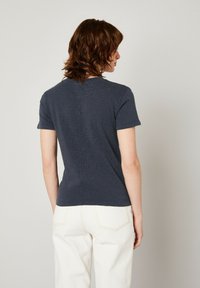 Tumši zilas krāsas īsām piedurknēm t-krekls ar apaļu apkakli, ar strukturētu virsmu un šuvju detaļām aizmugurē. Saskaņots ar baltām biksēm.