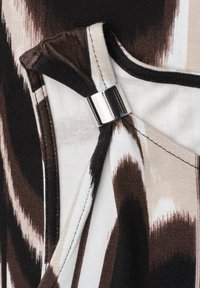 Gros plan d'un tissu avec des motifs abstraits marron et beige et un anneau en métal argenté qui maintient des couches de tissu pliées.