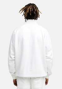 Weißer Fleece-Pullover mit hohem Kragen und langen Ärmeln, mit lockerem Schnitt und gerippten Bündchen, kombiniert mit passenden Hosen.