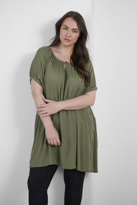 Robe tunique vert olive avec des manches courtes, un décolleté en rond avec un détail en trou de serrure, et une silhouette fluide. Associée à un pantalon noir.