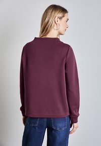 Felpa viola dal fitting rilassato, con maniche lunghe e scollo tondo. Abbinata a jeans denim blu scuro.