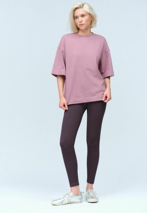 Överdimensionerad mauve t-shirt i mjuk bomull, kombinerad med tighta, mörk lila ribbade leggings och ljusgrå sneakers.