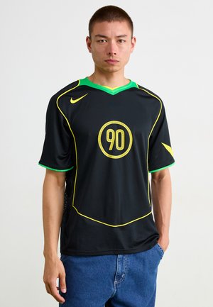Jersey deportivo negro de manga corta, con acentos amarillos y logotipo, cuello verde, que presenta un diseño circular con el '90' en el centro.