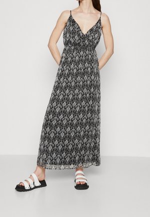 Robe maxi à motif noir et blanc avec un décolleté en V et de fines bretelles ; associée à des sandales à trois brides noires et blanches.