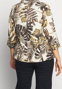 Bluse med krave og blomsterprint i creme med gule, sorte og brune bladmotiver; trekvartærmer; afslappet pasform; letvægtsstof.