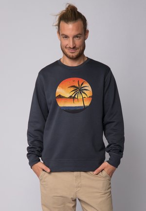 Marine sweatshirt met een ronde zonsondergang graphic met een palmboom, bergen en oceaan. Katoenen materiaal met ribbels aan de mouwen en onderrand.