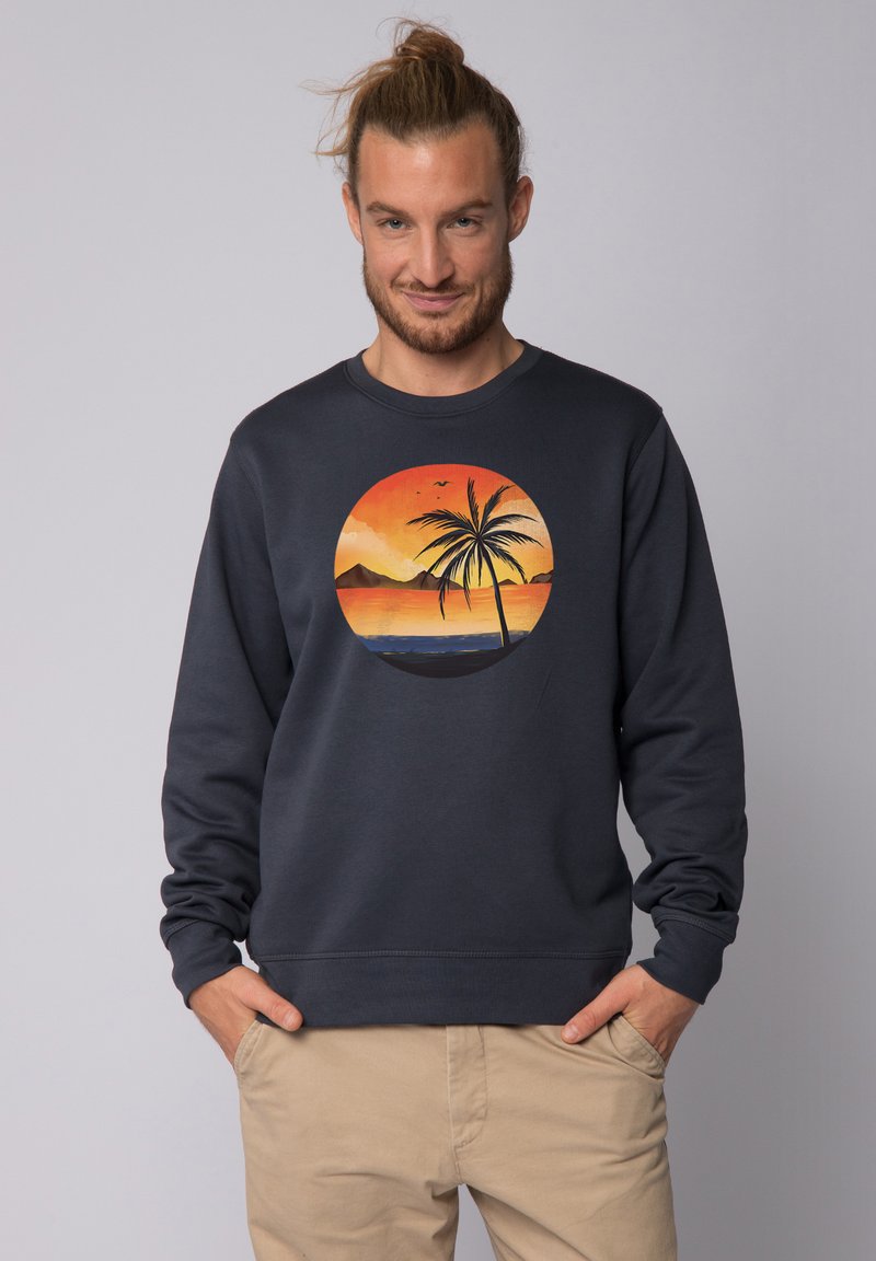 Marineblaue Sweatshirt mit einem runden Sonnenuntergangs-Graphic, das eine Palme, Berge und den Ozean zeigt. Aus Baumwollmaterial mit gerippten Bündchen und Saum.