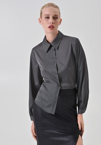 Camicia con bottoni bianca e nera con un motivo a righe, caratterizzata da un colletto a punta e maniche lunghe. Abbinata a una gonna nera elegante.