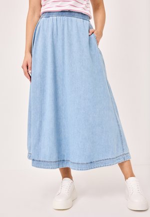 Light blue denim maxi skirt with an elastic waistband, side pockets, and a straight silhouette. Worn with white sneakers.