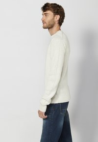 Ribbed kötött pulóver krém színben, kerek nyakkivágással és hosszú ujjal, sötétkék farmerral párosítva. Minimalista dizájn, texturált anyag.