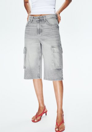 Shorts cargo en denim gris avec deux poches avant, ourlet effiloché et coupe décontractée, associés à des tongs rouges.