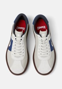 Zapatilla blanca y azul con parte superior de cuero liso, puntera redonda, suela de goma marrón contrastante y plantilla roja con el logotipo "CAMPER".
