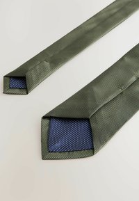 Grüne strukturierte Krawatte mit einer gepunkteten navyblauen Fütterung an den Enden; quadratisch geschnittene Spitzen. Verfügt über einen subtilen Glanz und ein leichtes Material.