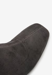 Grijze suède schoen met een vierkante neus en zichtbare stiksels langs de naad. Gladde textuur met een matte afwerking.