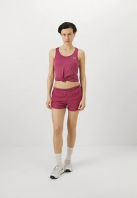 Lila sportlinne knutet vid midjan, kombinerat med matchande shorts med svart midjeband. Modellen bär vita strumpor och sneakers.