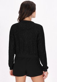 Schwarze, cropped Jacke aus strukturiertem Stoff mit geripptem Kragen und Bündchen. Das Design enthält subtilen Schimmer und eine taillierte Silhouette.