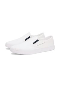 Paire de baskets blanches sans lacets avec élastique latéral et petit logo Tommy Hilfiger sur le côté extérieur de chaque chaussure.