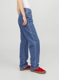 Jeans de denim azul claro com um corte reto, apresentando bolsos clássicos e uma textura ligeiramente desbotada. Usados com ténis vermelhos.