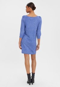 Robe en tricot bleu vif avec des manches trois-quarts, un col rond et une silhouette ajustée. Associée à des bottines noires.