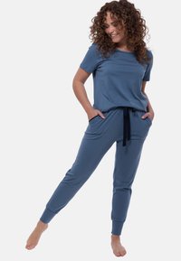 Sininen loungewear-setti, joka sisältää lyhyth anteen paidan ja kapeat housut, joissa on taskut, nyöritetty vyötärö ja pehmeä, kevyt kangas.