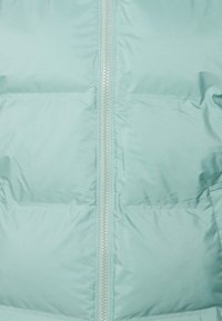 Tissu matelassé bleu clair avec une fermeture éclair centrale argentée, montrant une texture rembourrée et des lignes de couture horizontales.