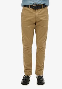 Khaki chino's met een rechte pasvorm, soepel materiaal, zijzakken en een discreet achtervak, gedragen met zwarte instappers en een zwarte riem.