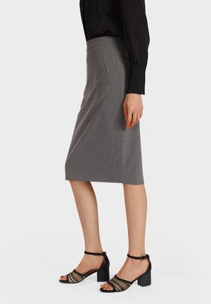 Donna che indossa una gonna a matita grigia fino al ginocchio, una camicetta nera a maniche lunghe e sandali neri con tacco a blocco e cinturini alla caviglia.