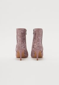 Botine cu dantelă în nuanță de mauve, cu toc, având un accent de suede roz neted la bază și o suprapunere decorativă din dantelă florala.