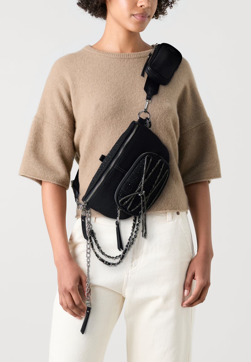 Zwarte schoudertas van gestructureerde stof, met een ritssluiting, kettingaccenten en een kleinere afneembare tas aan de schouderband.