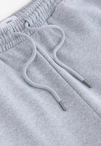 Graue Jogginghose mit elastischem Bund, Kordelzug mit Metallenden und weichem, gebürstetem Material. Logosticker sichtbar am Bund.