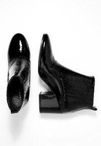 Botas de tobillo negras de cuero brillante con un panel lateral texturizado. Presentan una puntera redondeada y un tacón grueso.
