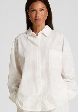 White button-up shirt made from textured fabric, featuring a chest pocket, collar, and slightly oversized fit.
