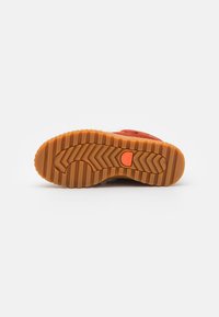 Suela de zapato de gamuza naranja con goma texturizada. Presenta un dibujo de patrón para agarre, con un logotipo redondo en el centro y un diseño general curvado.