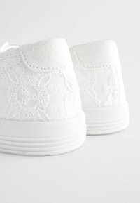 Fehér sneakers, hímzett virágmintával, vászon anyagból, és gumi talppal, vízszintes csíkokkal. Alacsony felsőrész.