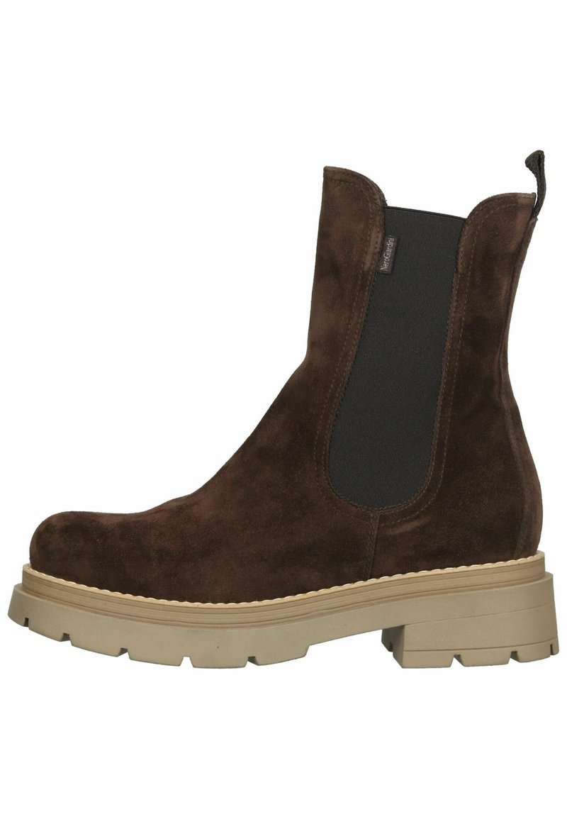 Botas Chelsea de ante marrón con paneles laterales elásticos, suela de goma marrón y detalles de costura a lo largo del borde. Diseño de punta redondeada y voluminoso.