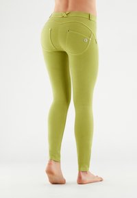 Leggings verdi con un design aderente, dotati di tasche posteriori e dettagli di cucitura discreti, realizzati in un materiale morbido e elasticizzato.
